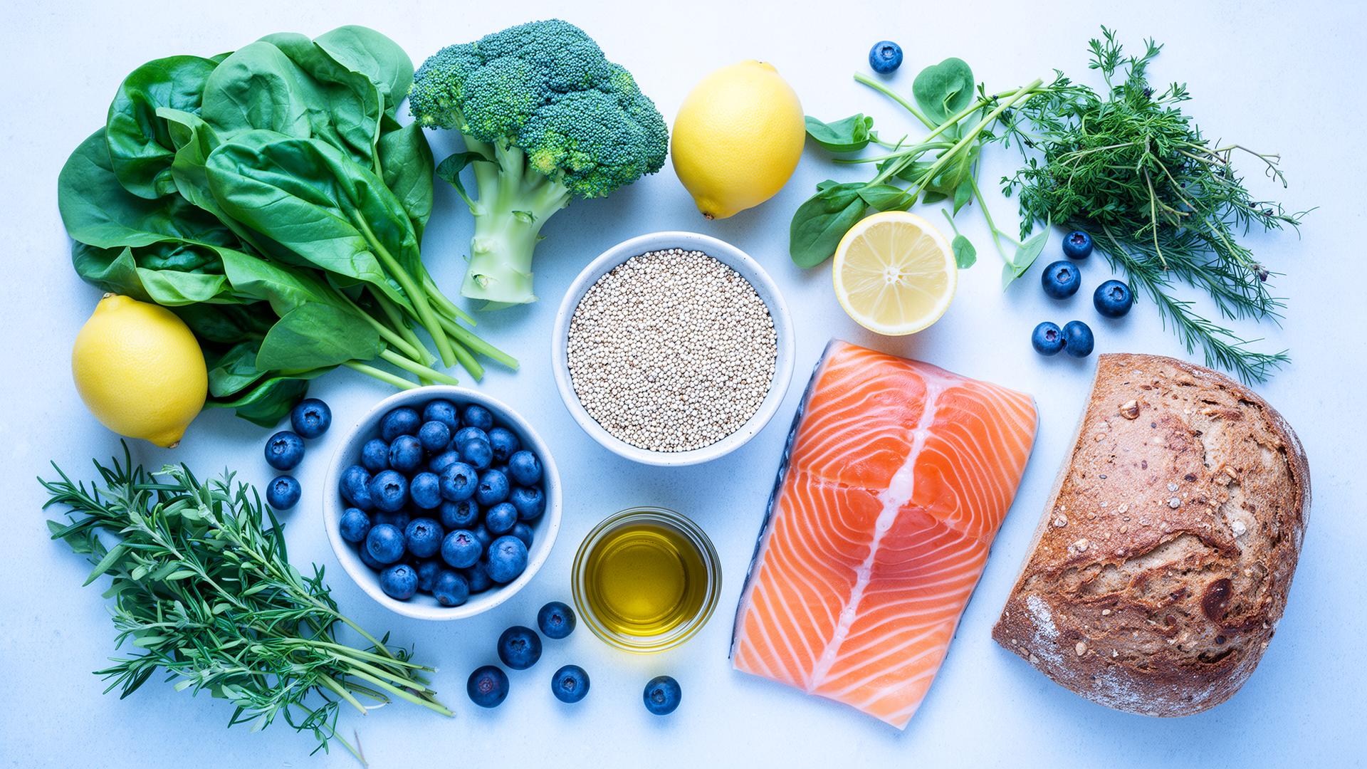 Fresh ingredients on a cool surface — greens, broccoli, blueberries, quinoa, salmon